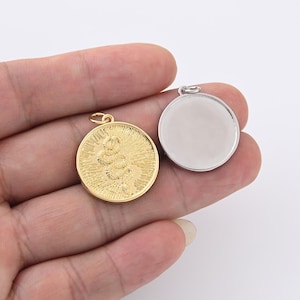 以下が含まれることがあります： 2つの丸いペンダント。1つは金色の色で、中央に詳細なヘビのデザインと、その周りにサンバーストパターンがあります。もう1つのペンダントは銀色で空白です。どちらにも、チェーンやその他のジュエリーに取り付けるための小さなループが付いています。