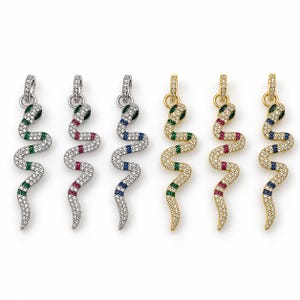 Pode incluir: Seis pingentes em forma de cobra com cristais transparentes em pavé e faixas de cristais verdes, vermelhos ou azuis. Três pingentes são prateados e três dourados, cada um com uma argola circular no topo para prender a uma corrente.