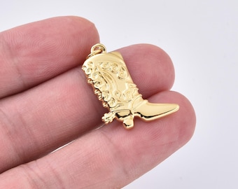 Puede incluir: Un dije dorado con forma de bota de vaquero. La bota tiene intrincados detalles en relieve en la caña y una punta puntiaguda. El dije tiene un pequeño lazo en la parte superior para sujetarlo a un collar o pulsera.