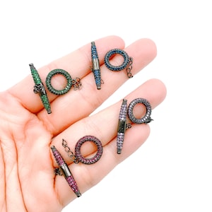 May include: Four toggle clasps with a black metal base and a round ring. Each clasp is adorned with colorful rhinestones, including green, blue, pink, and purple.