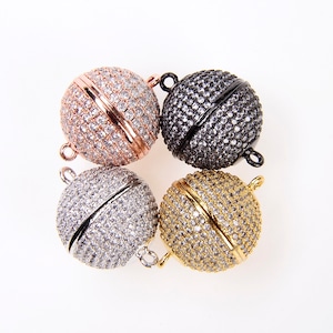 May include: Four round magnetic clasps for jewelry making. The clasps are made of metal and have a pave setting of clear rhinestones. The clasps are available in gold, silver, rose gold, and black.