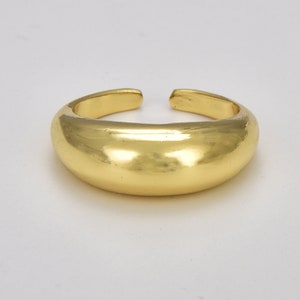 May include: A gold-colored ring with a smooth, rounded surface. The ring is made of metal and has a simple, minimalist design.