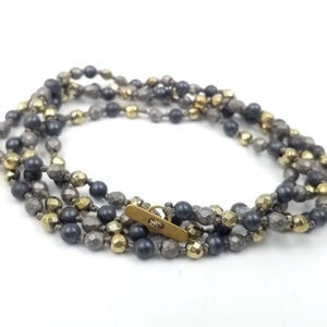 May include: A multi-strand necklace made of dark gray, light gray, and gold beads. The necklace has a brass clasp.
