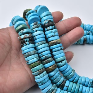 May include: A strand of turquoise beads shaped like flat discs. The beads feature a vibrant sky blue color with natural dark brown and black matrix veining throughout. The stones are arranged in a continuous line, showcasing varied textures and patterns.