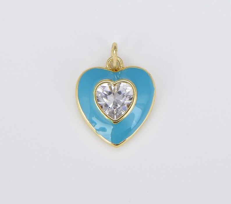 May include: A gold heart-shaped pendant with a clear crystal in the center. The heart is outlined in gold and filled with a light blue enamel.