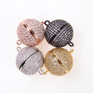 May include: Four round magnetic clasps for jewellery making. The clasps are made of metal and have a pave setting of clear rhinestones. The clasps are available in gold, silver, rose gold, and black.