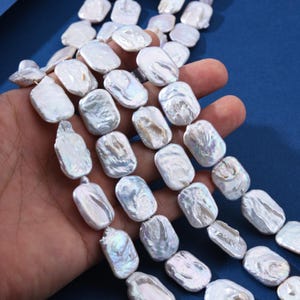 May include: A strand of white freshwater pearl beads, each bead is square shaped with a slightly irregular, natural form. The pearls have a subtle iridescent sheen.