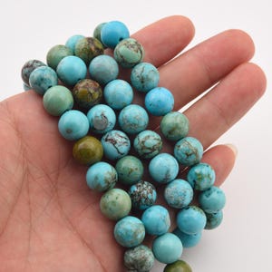 May include: A collection of round turquoise beads in varying shades of blue and green. The beads have a mottled appearance, with darker veins and spots. The beads are approximately 10mm in diameter, perfect for jewelry making.