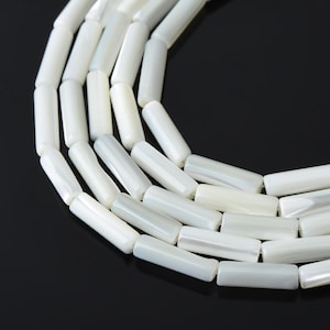 May include: Close-up of a strand of white, cylindrical beads. The beads have a pearlescent sheen and are arranged in a curved pattern against a black background. The beads are uniform in size and shape, suggesting they are for jewelry making.