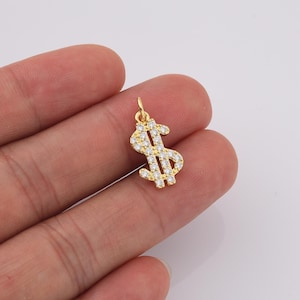 May include: Gold-tone pendant charm in the shape of a dollar sign, encrusted with clear cubic zirconia stones.