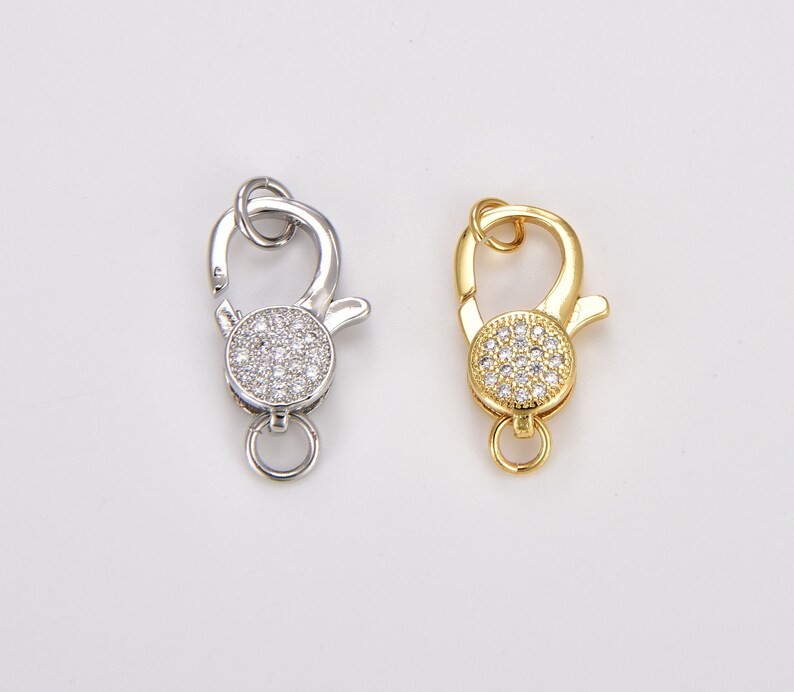 May include: Two silver and gold lobster clasps with clear crystal accents. The clasps are round and have a small loop on the side.