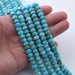 May include: Strands of turquoise-colored, faceted gemstone beads. The beads have a hexagonal shape and are strung together. The color is a vibrant blue-green with brown matrix patterns. The beads are held in a hand.