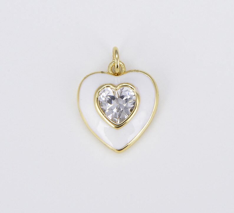 May include: A gold heart-shaped pendant with white enamel and a clear rhinestone in the center.