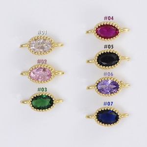 Könnte beinhalten: Sieben goldfarbene ovale Charms mit verschiedenen farbigen Edelsteinen. Die Charms sind von #01 bis #07 nummeriert. Die Edelsteine sind rosa, weiß, grün, rot, schwarz, lila und blau.