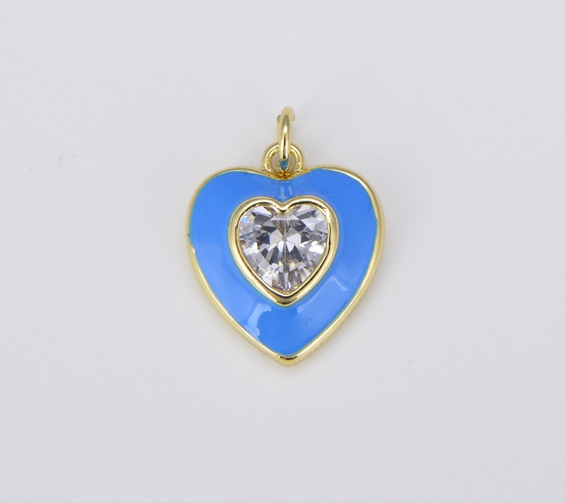 May include: A gold heart-shaped pendant with a clear crystal in the center. The heart is outlined in gold and filled with a light blue enamel.