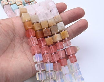 Peut inclure: Plusieurs rangées de perles de pierres précieuses cubiques dans des tons de rose, orange, jaune et bleu. Les perles sont enfilées et tenues dans une main. Idéal pour la création de bijoux.