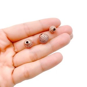 May include: Three rose gold-toned beads with clear rhinestones. The beads are different sizes and are perfect for jewelry making.