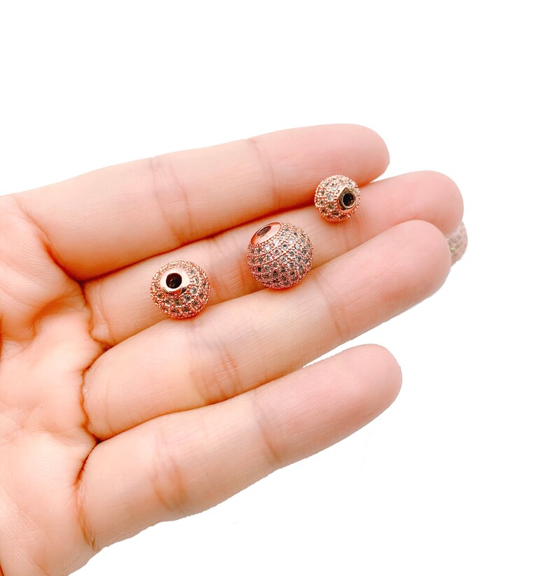 May include: Three rose gold-toned beads with clear rhinestones. The beads are different sizes and are perfect for jewelry making.