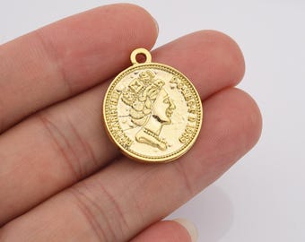 May include: Gold-colored metal pendant charm featuring a profile of a woman wearing a crown. The pendant is round and has the text "DUCIBUS D 1980" around the edge.