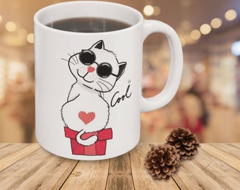 May include: White ceramic mug with a cartoon illustration of a cat wearing sunglasses and a red heart on its chest. The cat is sitting in a red box with white polka dots. The text "be Cool" is written on the mug.