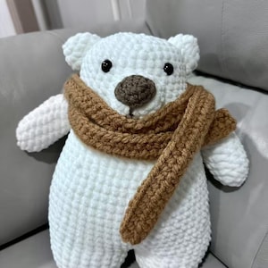 May include: A handmade white crochet bear with a brown nose, black eyes, and a brown scarf. The bear has small ears and arms, and is sitting upright. The soft toy is a cozy, handmade item.