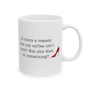 Könnte beinhalten: Eine weiße Kaffeetasse mit schwarzem Text, der lautet: "Gibt es einen Grund, warum mein Kaffee nicht da ist? Ist sie gestorben oder so?" Ein roter High-Heel-Schuh ist neben dem Text abgebildet.