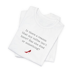 May include: White t-shirt with the text "Is there a reason that my coffee isn't here? Has she died or something?" and a red high heel graphic. The shirt is folded.
