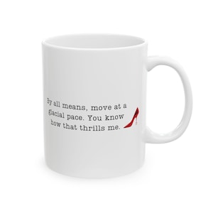 May include: White ceramic coffee mug with a black and red design. The mug features the text "By all means, move at a glacial pace. You know how that thrills me." and a red high heel shoe graphic.