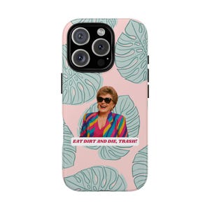 May include: A phone case featuring a smiling woman wearing sunglasses and a colorful blazer. The case has a pink background with green leaf patterns and the text "EAT DIRT AND DIE, TRASH!"