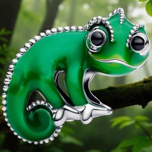 Puede incluir: Un charm de camaleón verde con base y detalles plateados. El charm está posado en una rama, sobre un fondo borroso de bosque. El camaleón tiene grandes ojos negros y un diseño detallado y texturizado.