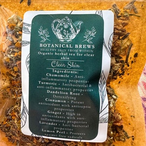 May include: A clear plastic bag filled with dried herbs and spices. A green and white label reads "Botanical Brews" and "Clear Skin." Ingredients include chamomile, turmeric, dandelion root, cinnamon, ginger, lavender, and lemon peel.