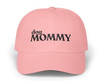 May include: A light pink baseball cap with the words "dog MOMMY" printed in black across the front. The cap has a curved brim and a rounded crown. This hat is a great gift for dog lovers.
