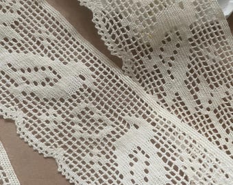 May include: Two pieces of white crocheted lace trim with a delicate pattern. The lace is soft and intricate, with a scalloped edge.