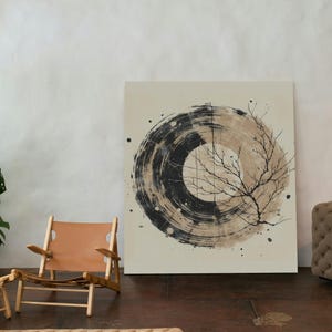 Op de afbeelding: Abstract kunstcanvas met een zwart en beige cirkelvormig ontwerp en een illustratie van een boomtak. Een lichtbruine leren stoel en een geweven vloerkleed staan op de voorgrond. Het kunstwerk wordt tentoongesteld in een kamer met een neutraal kleurenpalet.