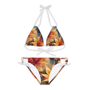 Pode incluir: Um biquíni branco com um top halter e uma parte inferior com laços ajustáveis. O tecido apresenta uma estampa de folhas de outono coloridas.