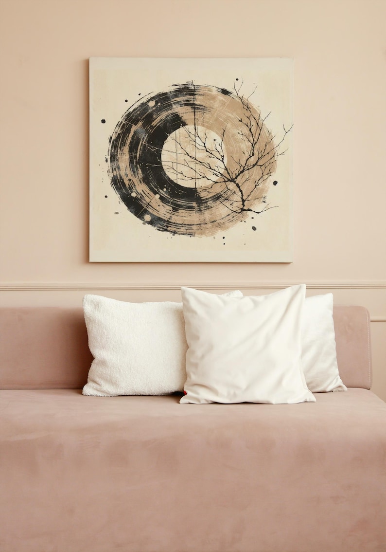 Op de afbeelding: Een vierkant canvas kunstwerk met een cirkelvormig abstract ontwerp in zwart- en bruintinten, met een illustratie van een boomtak. Daaronder een roze bank met drie witte kussens, een pluizige en twee gladde.