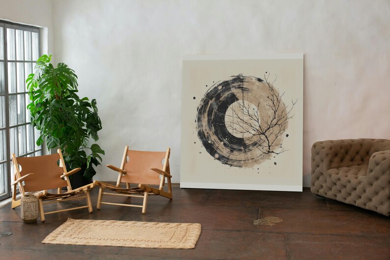 Op de afbeelding: Een abstracte kunstprint met een cirkelvormig ontwerp in zwart en beige en een takillustratie. Het kunstwerk staat in een kamer met twee houten stoelen met bruin lederen zittingen, een vloerkleed en een grote groene plant.