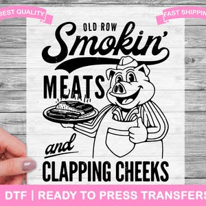 Op de afbeelding: Zwart-witte illustratie van een varken dat een schort draagt en een bord met ribben vasthoudt. De tekst "Old Row Smokin' Meats and Clapping Cheeks" staat boven het varken. De tekst "DTF | Ready to Press Transfers" staat onder het varken.