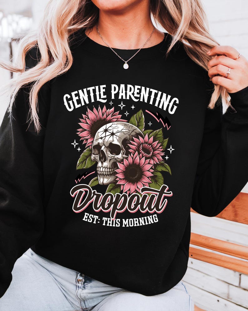 Op de afbeelding: Zwart sweatshirt met een schedel omringd door roze bloemen en de tekst "Gentle Parenting Dropout Est: This Morning".