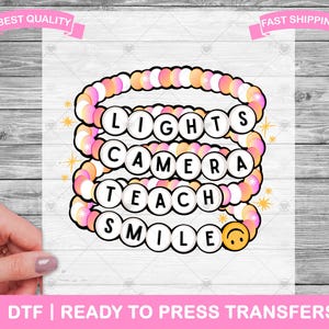 May include: A pink and white layered beaded bracelet with the words "Lights Camera Teach Smile" on it. The bracelet has a yellow smiley face charm.