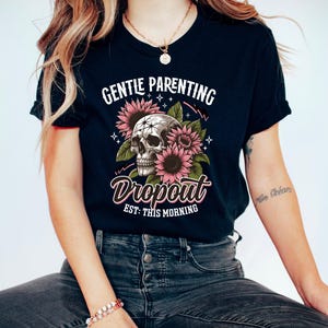 Op de afbeelding: Zwart T-shirt met een schedel en zonnebloemen afbeelding. De tekst "Gentle Parenting Dropout Est: This Morning" is op het shirt gedrukt.