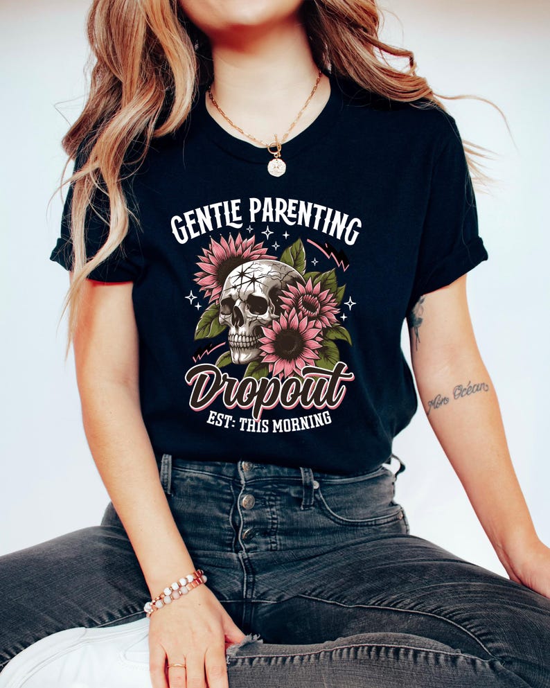 Op de afbeelding: Zwart T-shirt met een schedel en zonnebloemen afbeelding. De tekst "Gentle Parenting Dropout Est: This Morning" is op het shirt gedrukt.