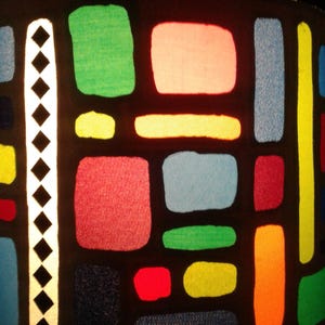 May include: A black lampshade with a geometric pattern of colourful squares and rectangles. The squares and rectangles are in shades of red, green, blue, yellow, and orange.