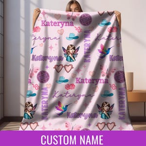 Op de afbeelding: Een lichtroze deken met een herhalend patroon van harten, vlinders, cowboyhoeden, dobbelstenen en de naam "Kateryna". De deken bevat ook illustraties van een fee en een kolibrie. De woorden "CUSTOM NAME" staan onderaan.