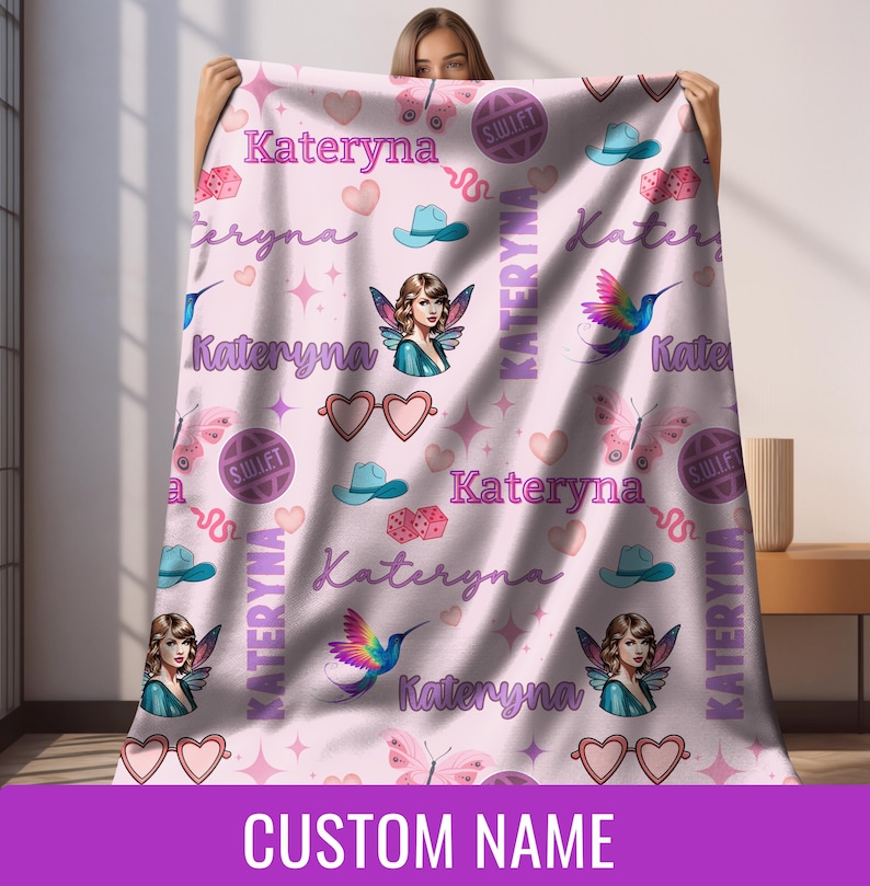 Op de afbeelding: Een lichtroze deken met een herhalend patroon van harten, vlinders, cowboyhoeden, dobbelstenen en de naam "Kateryna". De deken bevat ook illustraties van een fee en een kolibrie. De woorden "CUSTOM NAME" staan onderaan.
