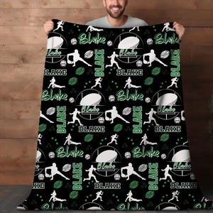Peut inclure: Couverture en polaire noire et verte avec un motif répété d'un ballon de rugby, d'un joueur courant avec le ballon et le nom "Blake" dans une police de caractères stylisée.