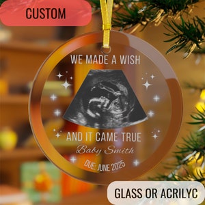 May include: A clear, round glass ornament with a gold ribbon for hanging. The ornament features an ultrasound image, the text "WE MADE A WISH AND IT CAME TRUE", a baby's name, and a due date. The word "CUSTOM" is at the top.