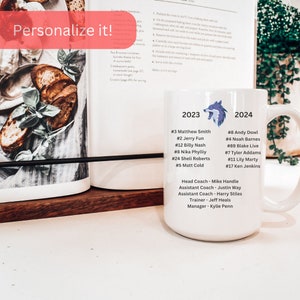 May include: White ceramic mug with a wolf design and text that reads "2023" and "2024". The mug lists names and numbers for a sports team, including the head coach, assistant coaches, trainer, and manager.
