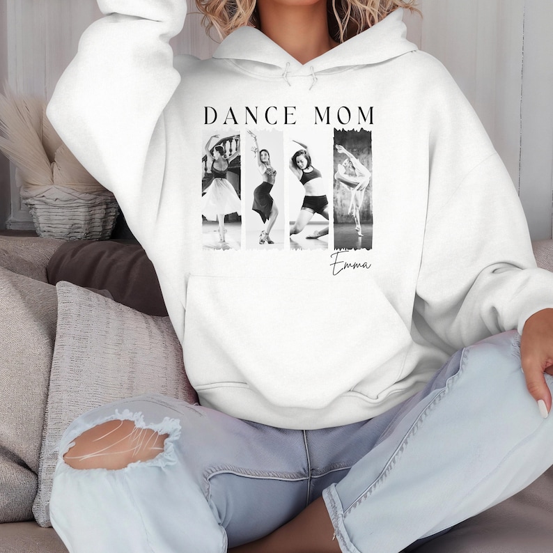 Peut inclure: Un sweat-shirt blanc avec l'inscription "DANCE MOM" au-dessus d'une image en noir et blanc de quatre danseuses. Le nom "Emma" est &eacute;crit en script en dessous de l'image. Le sweat-shirt a une poche avant et une capuche.