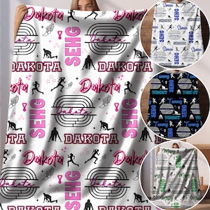 Puede incluir: Manta de forro polar blanca con un diseño de atletismo en rosa y negro. La manta presenta las palabras "Dakota SEHG" repetidas en todo el diseño.